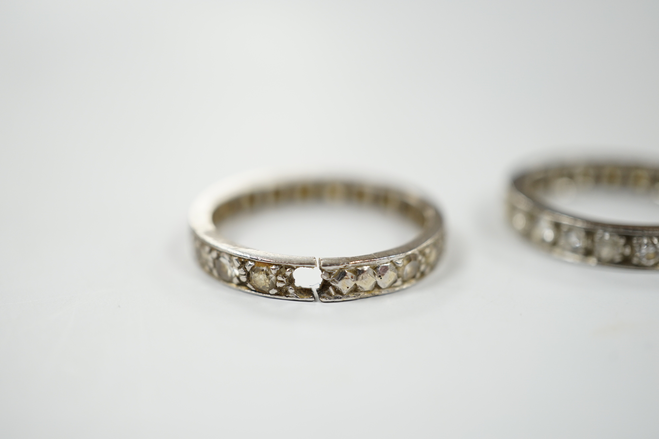 Two white metal and diamond set full eternity rings, one with cut shank and stone missing, sizes L & P, gross weight 7.7 grams.